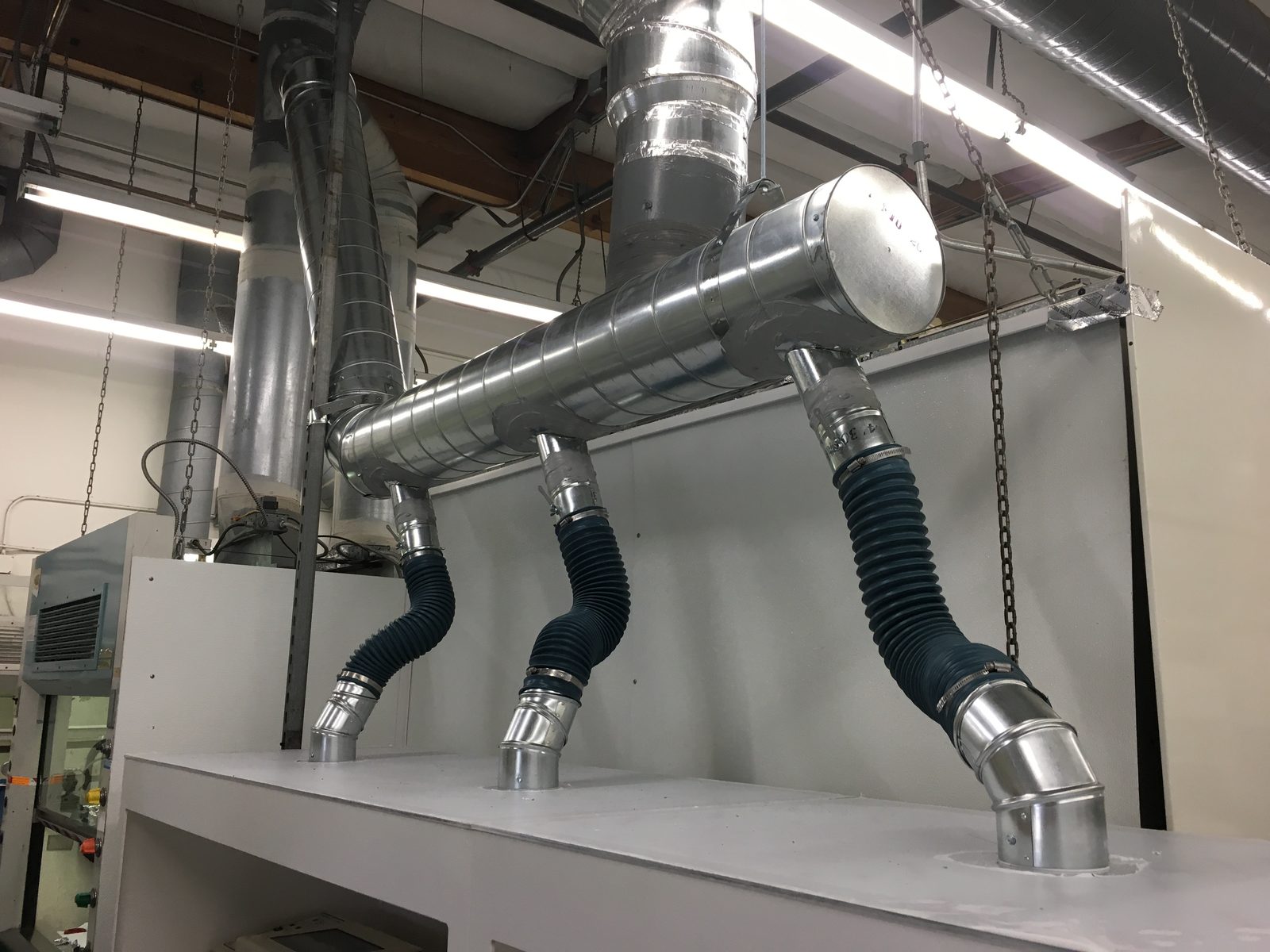 Source-capture exhaust arms and spiral ductwork above a laboratory bench