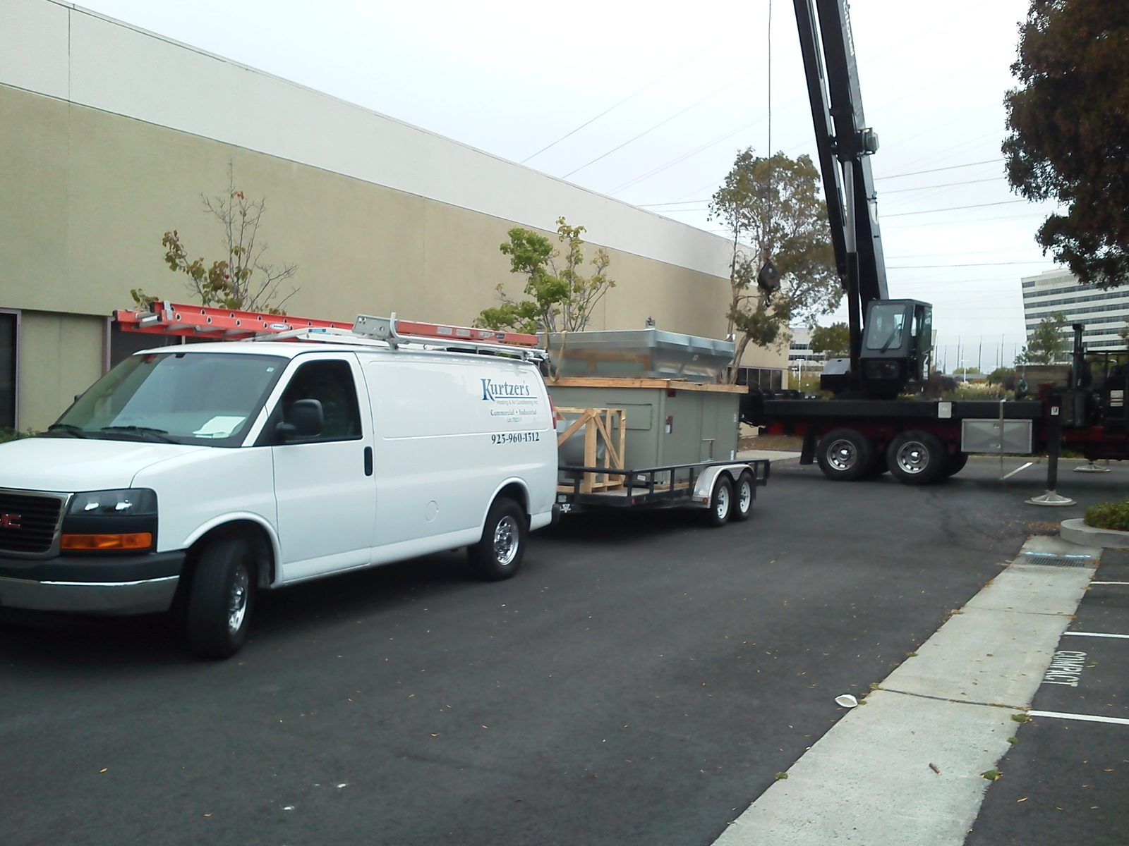 Service van and trailer with a new rooftop unit staged beside a crane
